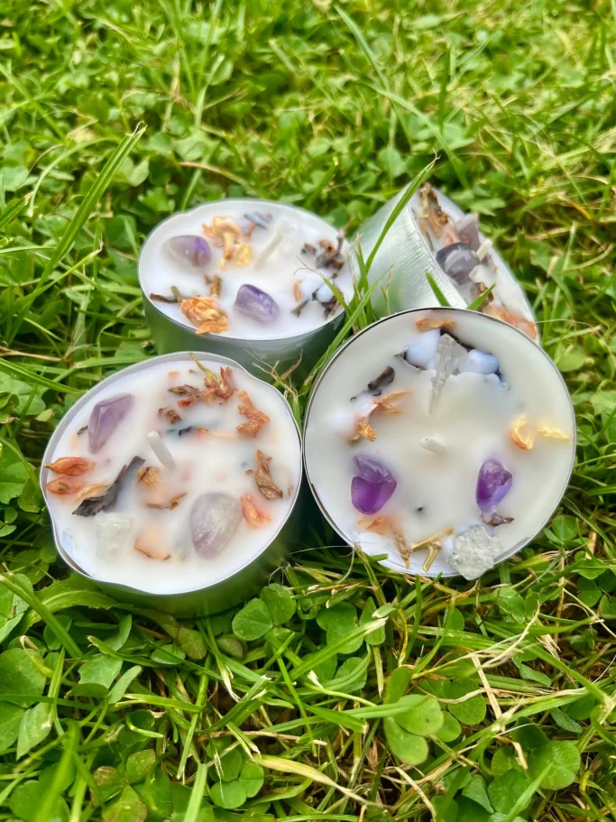 Vier runde Kerzen mit getrockneten Blumen und Kräutern auf grünem Gras.