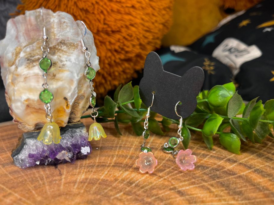 Bunte Ohrringe aus Silber mit grünen und rosafarbenen Blüten, auf einem Holzuntergrund.