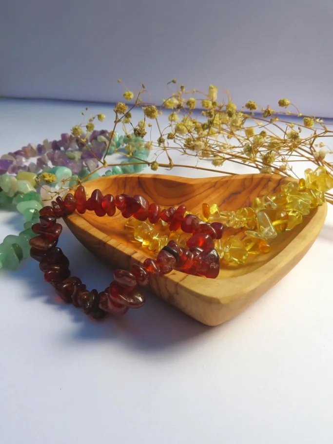 Holzschale mit bunten Kristallketten und getrockneten Blüten arrangiert.