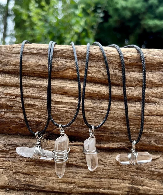 Mehrere Schmuckhalsketten mit klaren Kristallanhängern an schwarzen Schnüren.