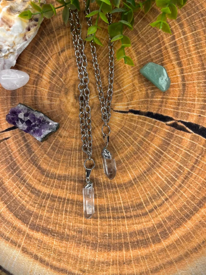 Silberne Kette mit zwei klaren Anhängern auf einem Holzuntergrund und bunten Steinen.