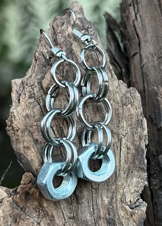 Silberne Ohrringe aus metallischen Ringen und einer Mutter, auf einem Holzuntergrund.