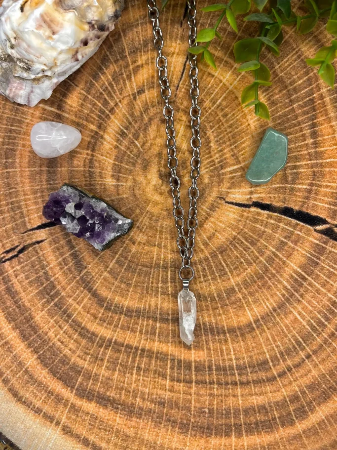 Eine Kette mit klarem Kristall, umgeben von verschiedenen Edelsteinen auf Holzuntergrund.