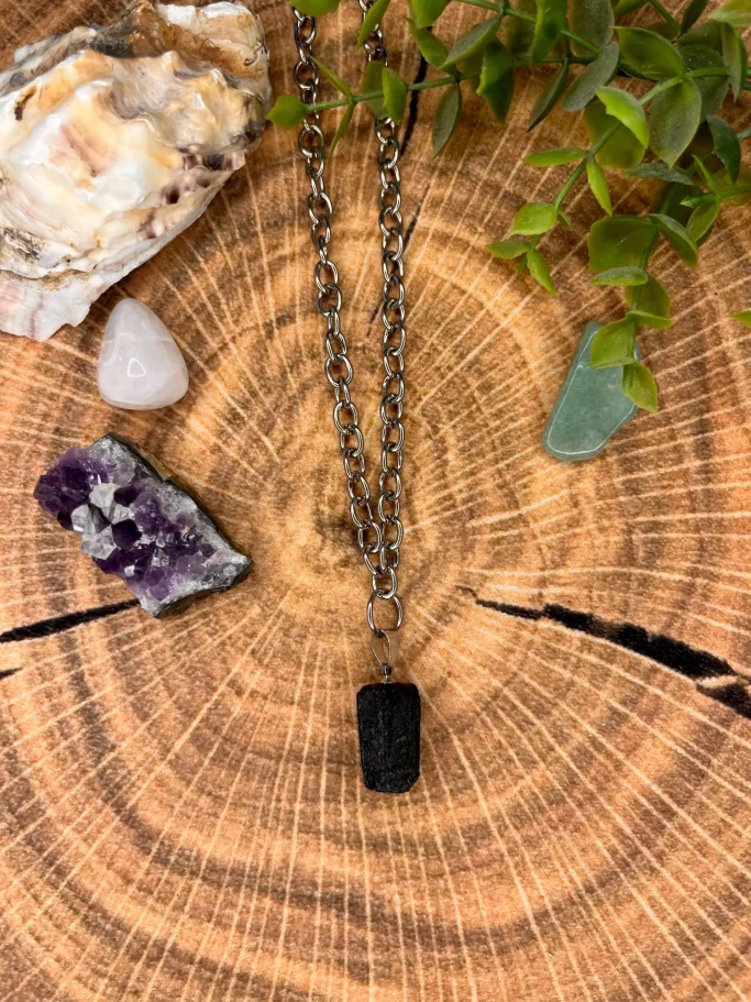 Schwarze Halskette mit einem rechteckigen Anhänger und bunten Steinen auf Holzuntergrund.