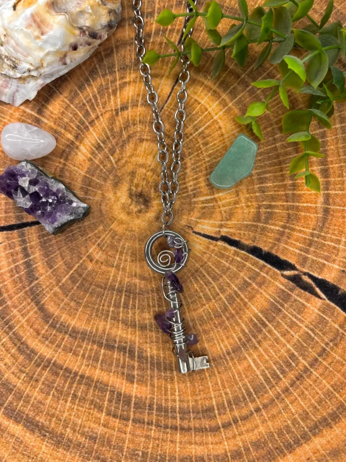 Ein schlichter Schlüsselanhänger mit Amethyst, umgeben von Edelsteinen auf Holzuntergrund.